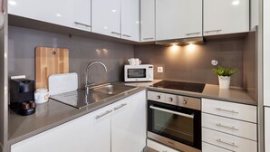 Una cocina moderna con armarios blancos, un lavamanos de acero inoxidable, un microondas, un horno y una tabla de cortar de madera.
