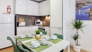 Una cocina moderna con armarios blancos, un microondas y un lavamanos. Hay una mesa de comedor dispuesta con cuencos, tazas y una planta.