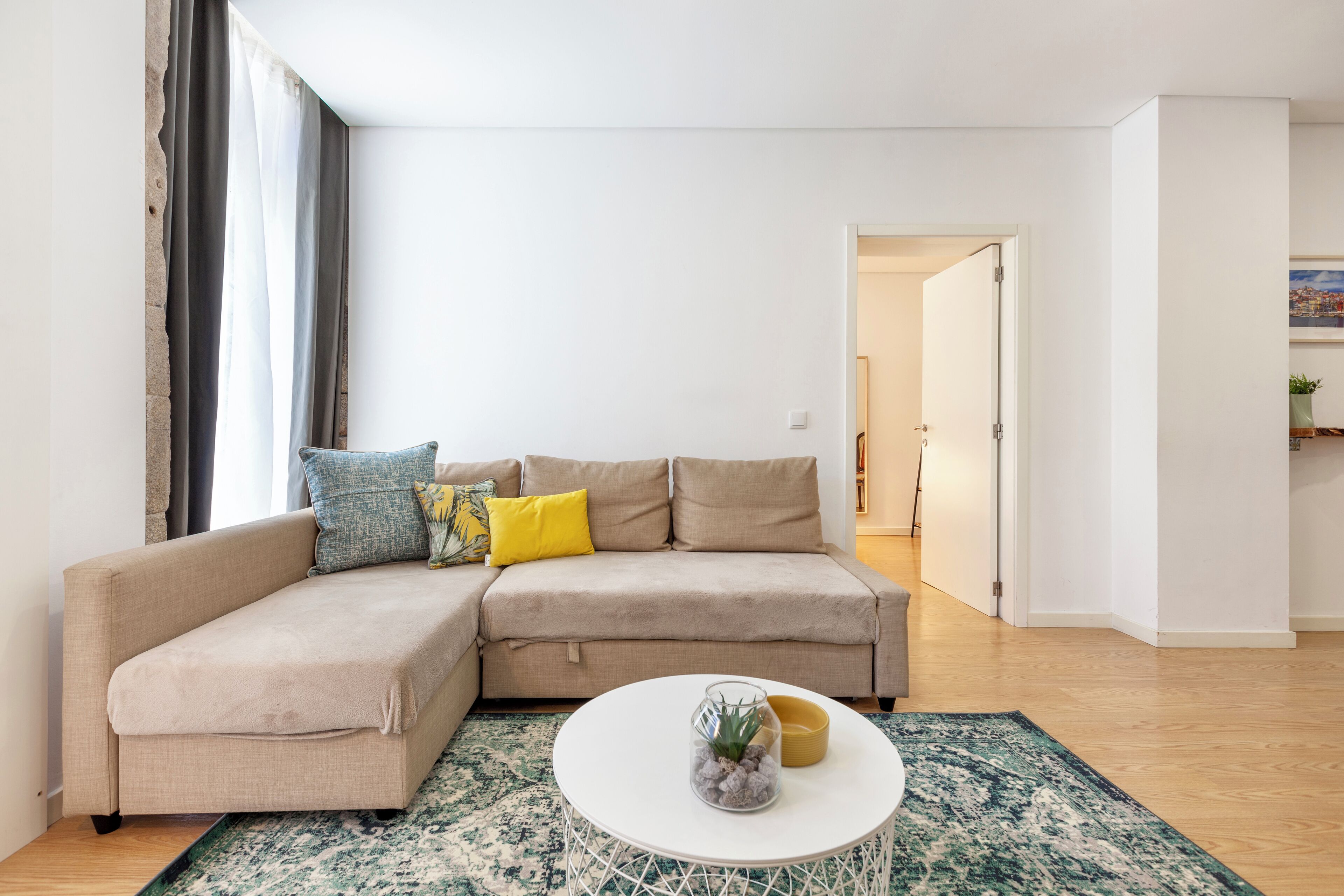 A modern living room with a beige sectional sofa, a round coffee table, and a patterned rug.