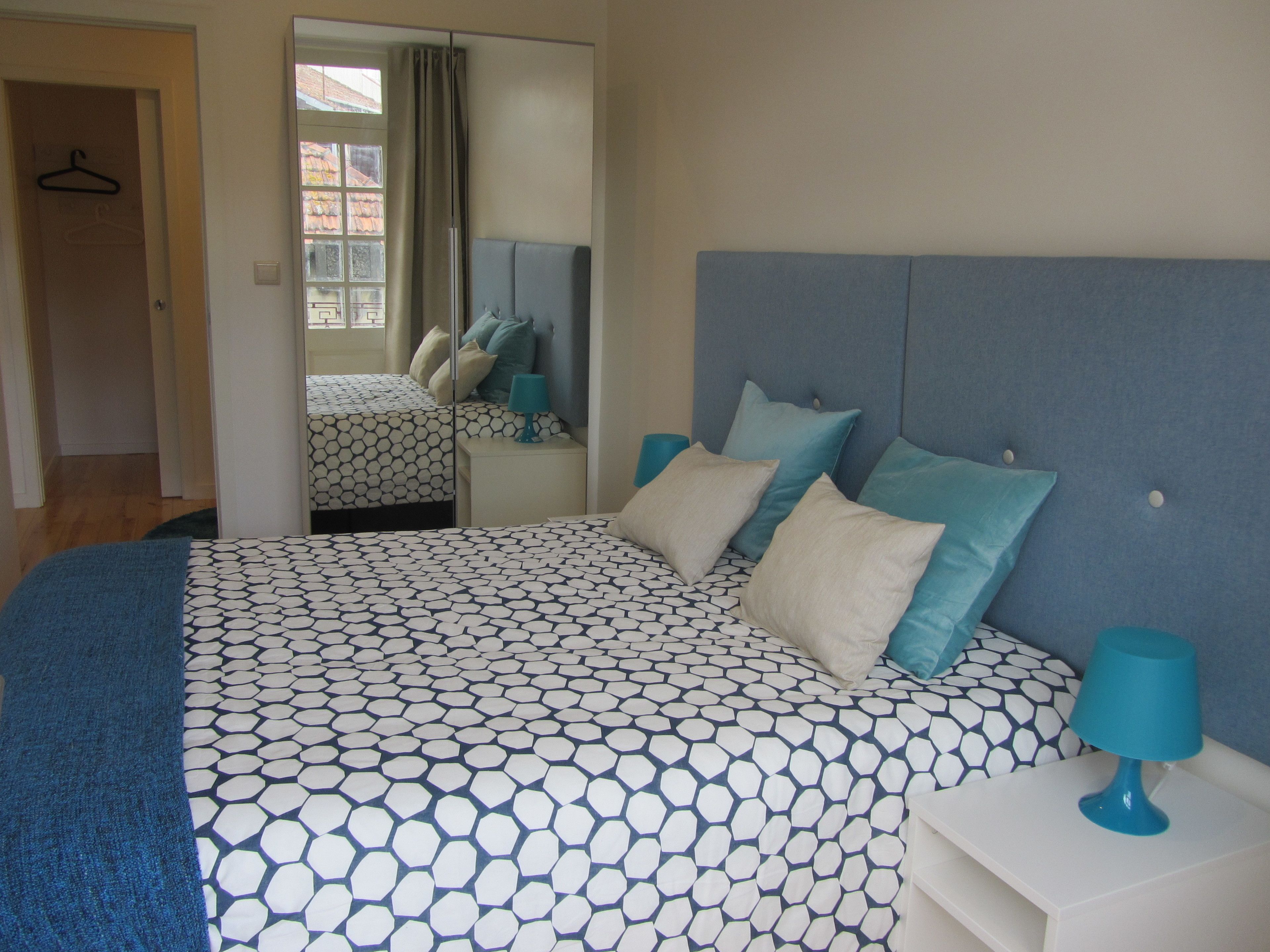 A bedroom with a bed, a nightstand, a mirror, and a door with a hanger.