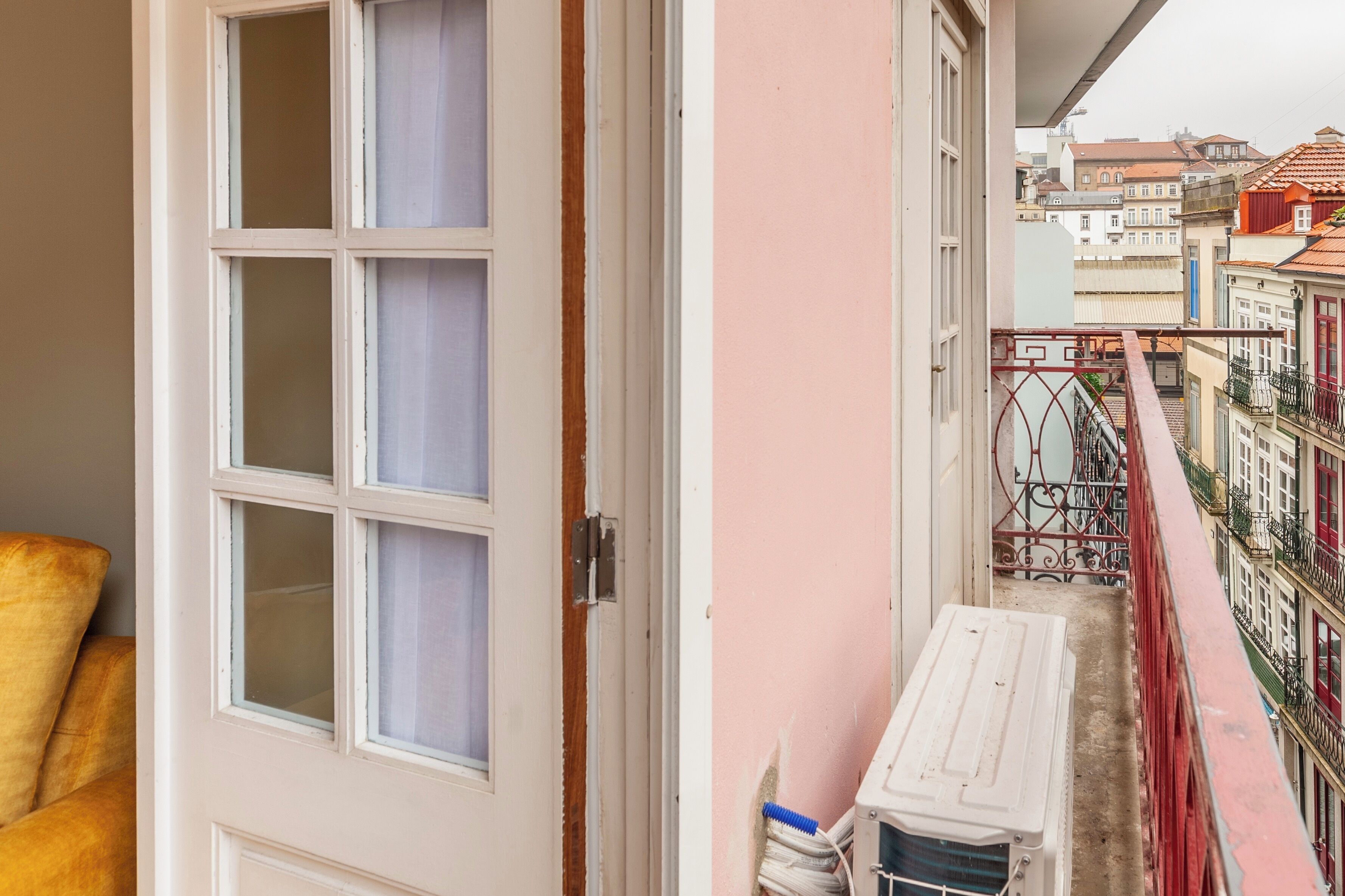 Een smalle gang met een deur die uitkomt op een balkon met uitzicht op een stadslandschap.