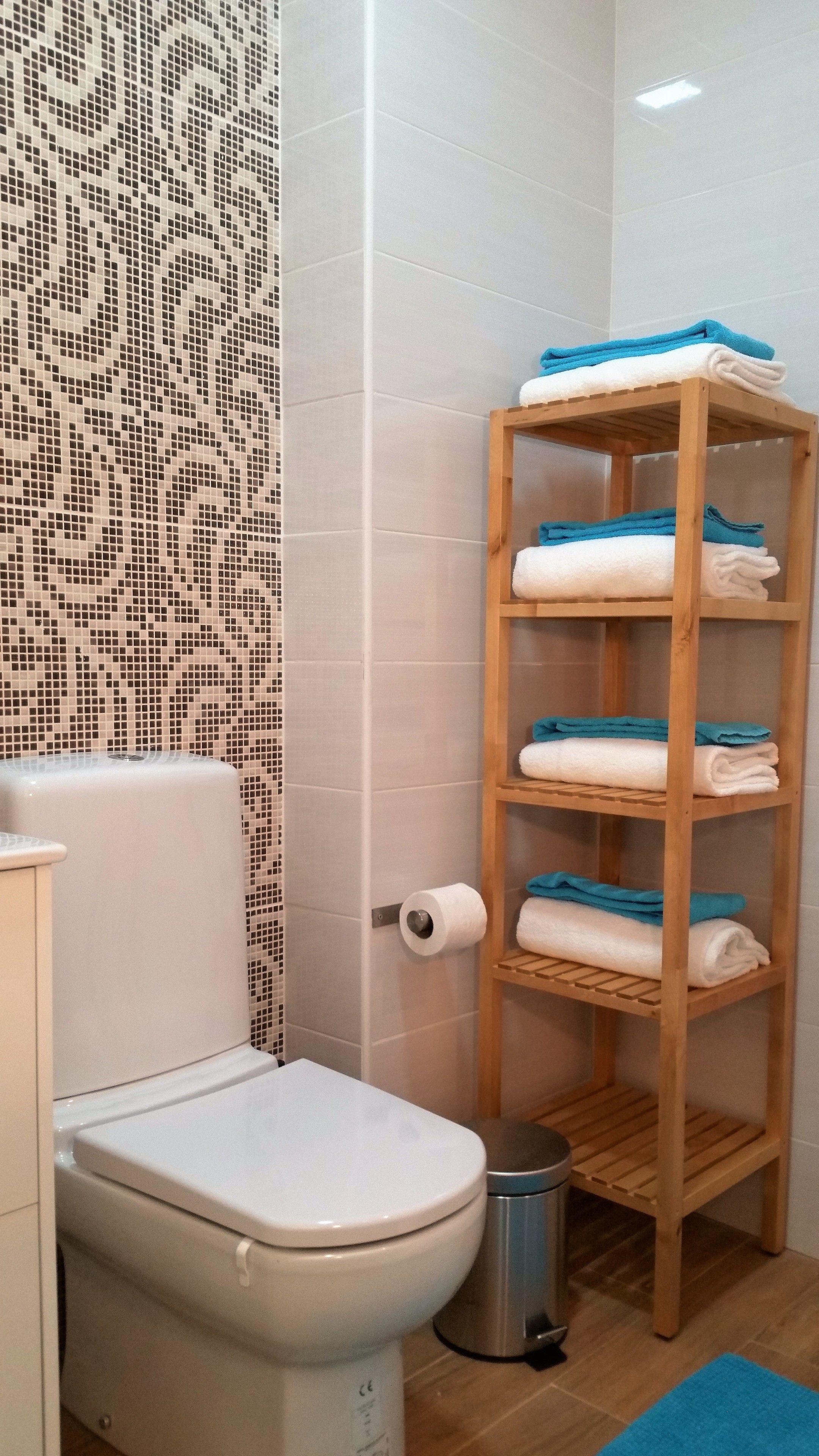 A bathroom with a toilet, a wooden shelf with towels, and a patterned wall.