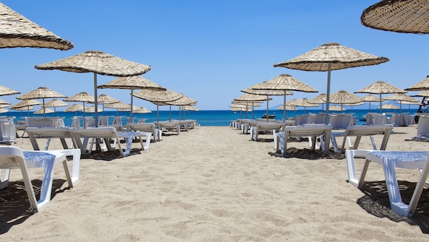 A beach with rows of white lounge chairs and thatched umbrellas, leading to the sea. - Musho Hotel (Ayvalik)