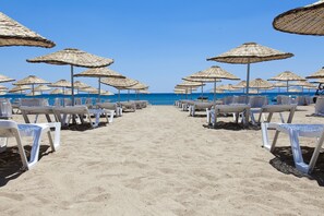 A beach with rows of white lounge chairs and thatched umbrellas, leading to the sea. - Musho Hotel (Ayvalik)