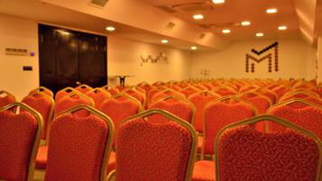 Rows of red chairs with gold frames in a conference room with a dark door and a wall with a geometric pattern.