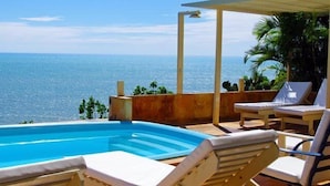 Ein Pool mit Meerblick, Liegestühle und ein überdachter Bereich mit Pflanzen.