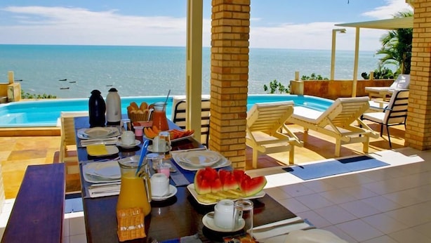 Ein Frühstückstisch mit Blick auf das Meer, einen Pool und Liegestühle.