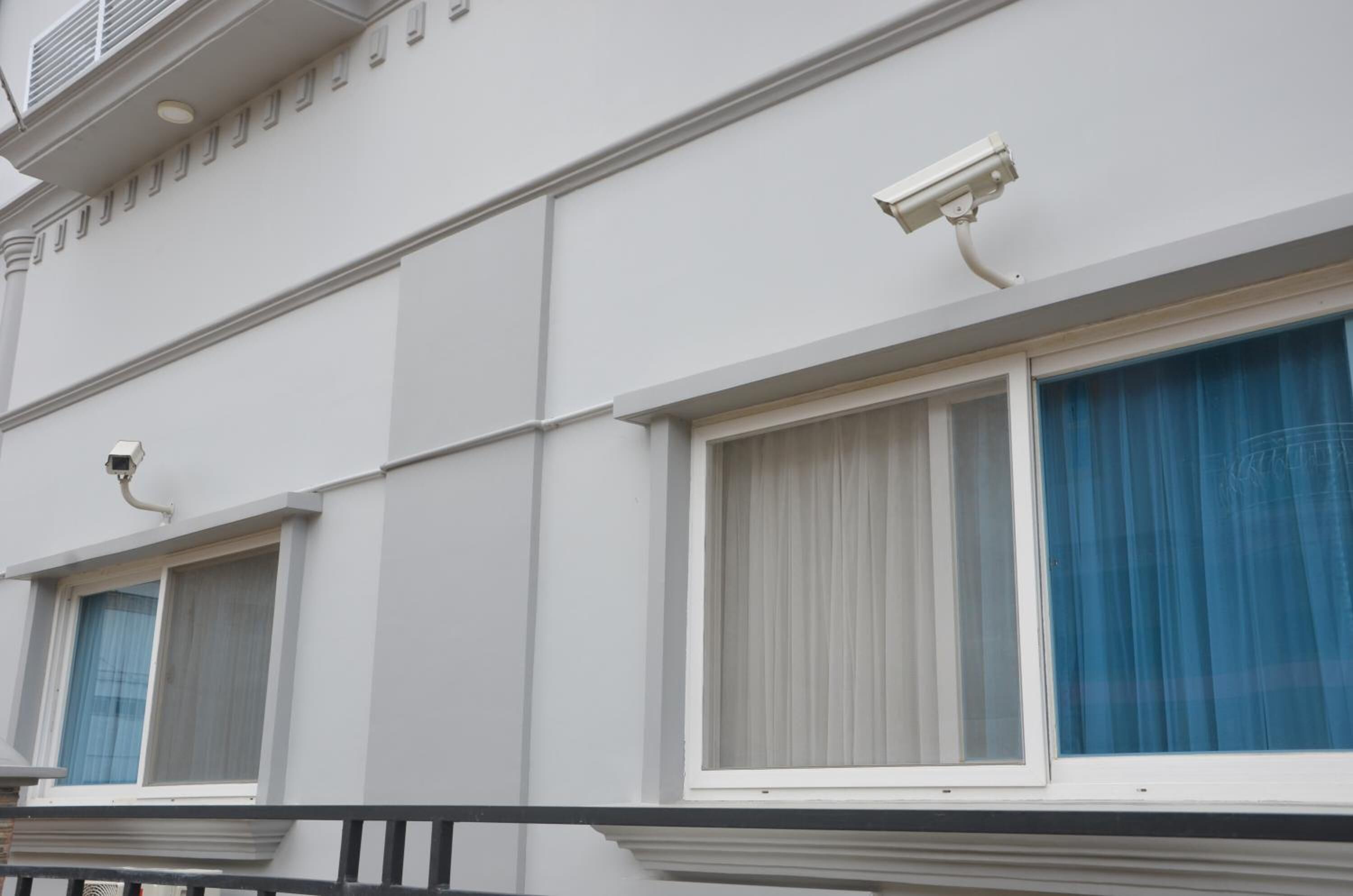 A building facade with three windows, each with a white frame and a security camera above.