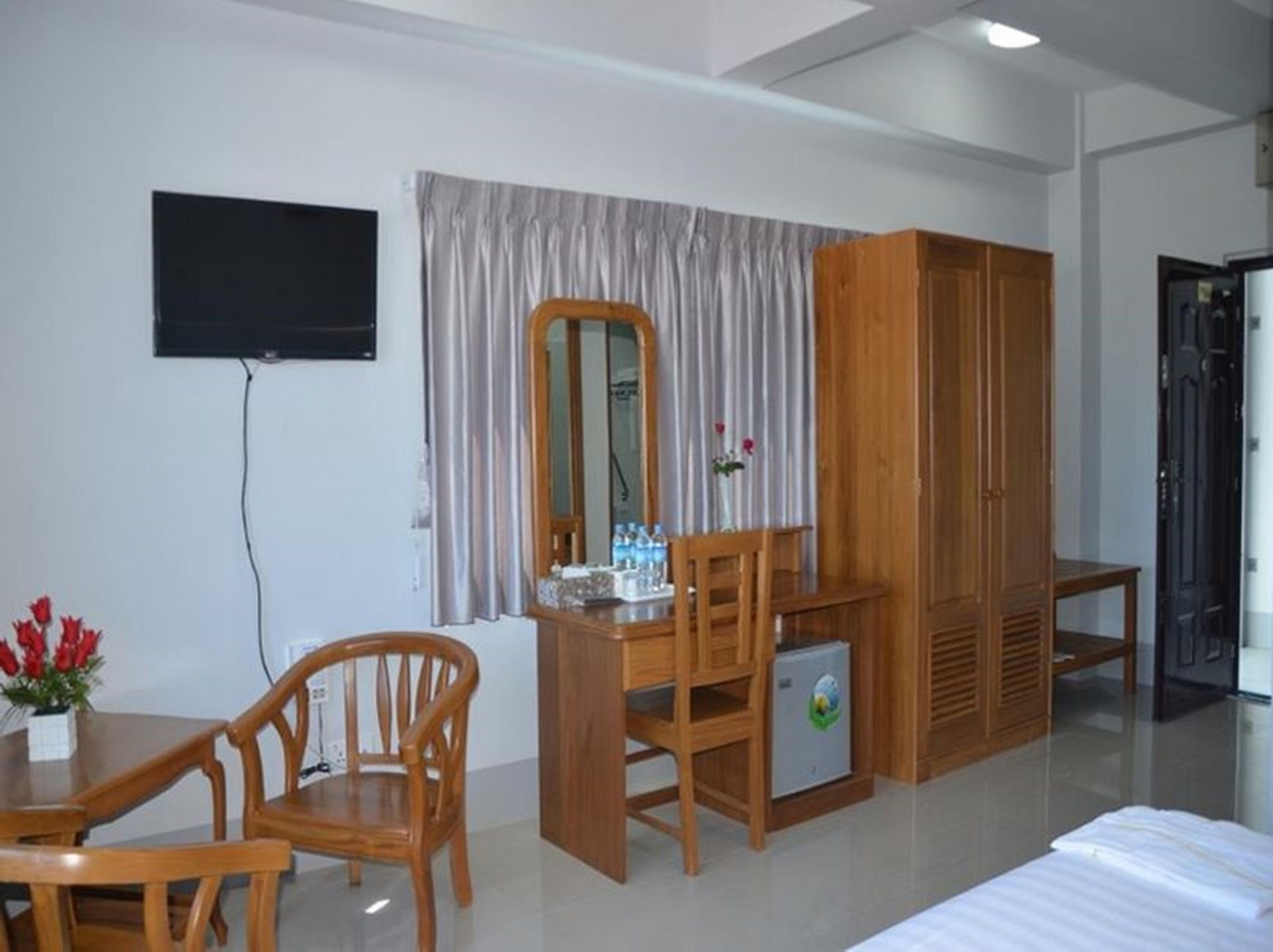 A hotel room with a bed, wooden furniture, a TV, a mirror, and a wardrobe.