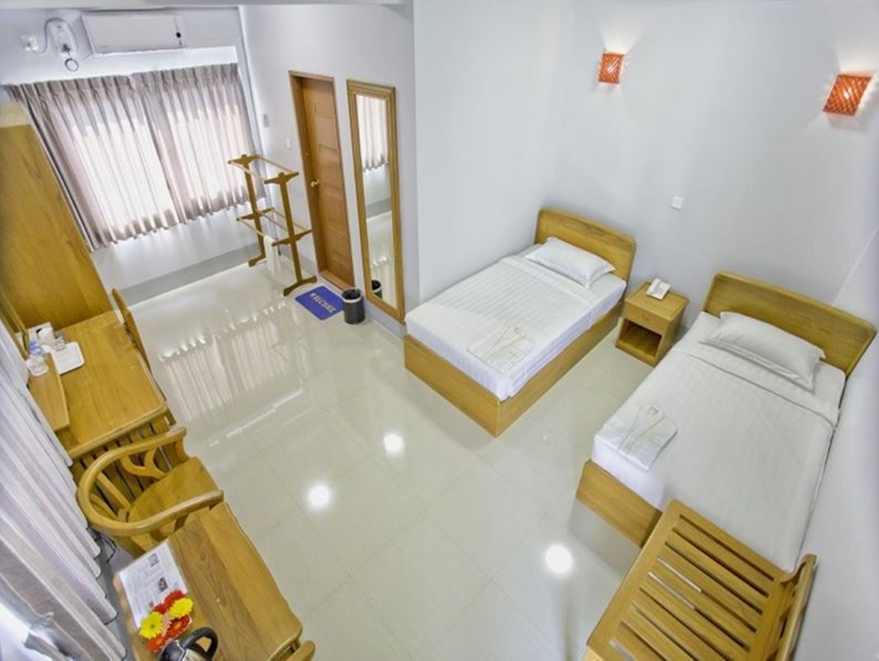 A hotel room with a wooden bed, a wooden desk, a chair, a small table, a mirror, and a window with curtains.