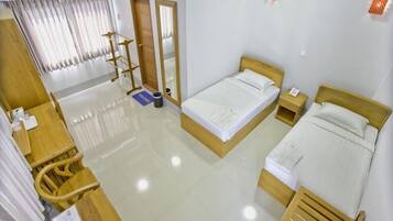 A hotel room with a wooden bed, a wooden desk, a chair, a small table, a mirror, and a window with curtains.