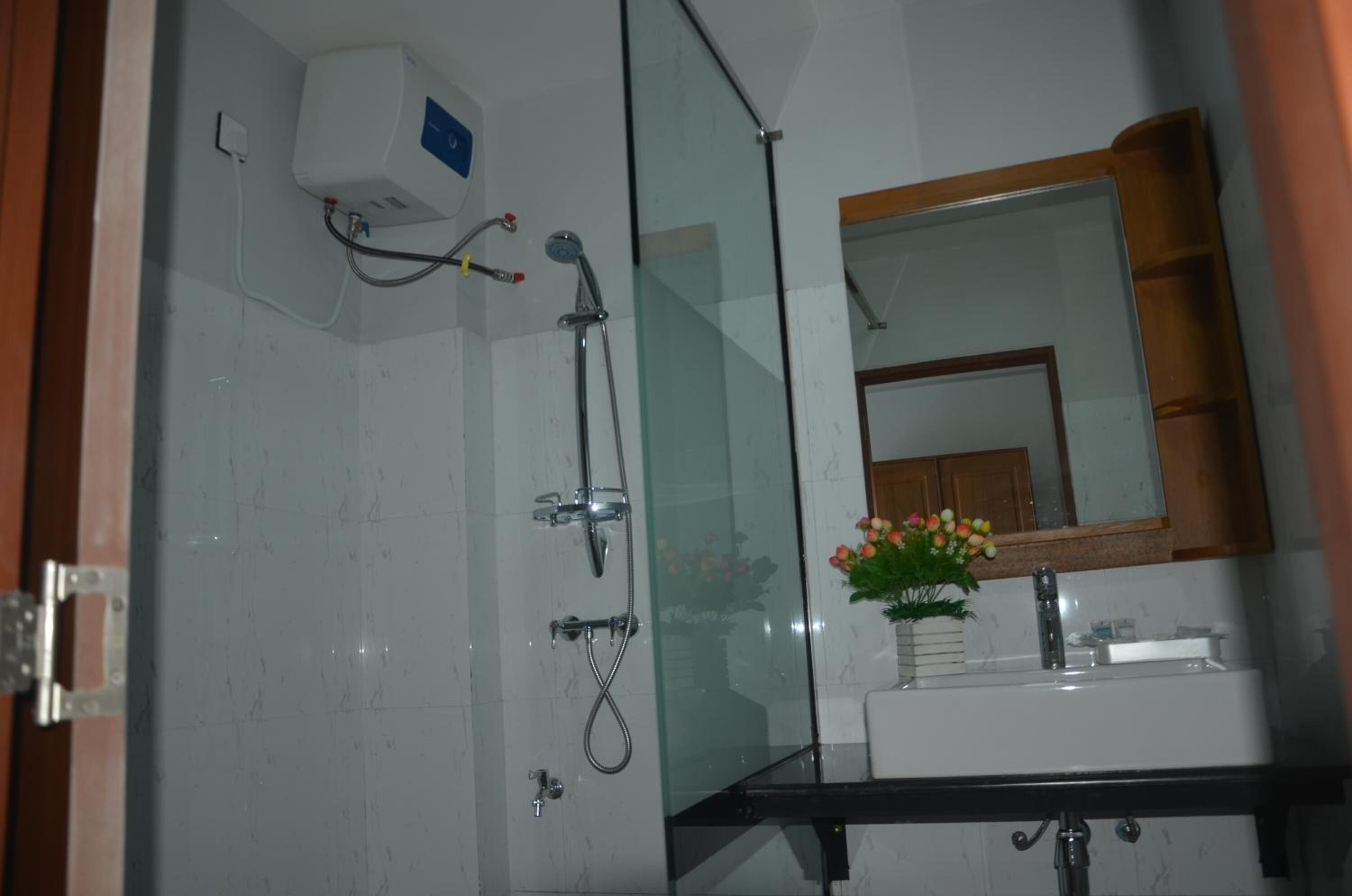 A bathroom with a glass shower enclosure, a white sink, a mirror, and a potted plant.
