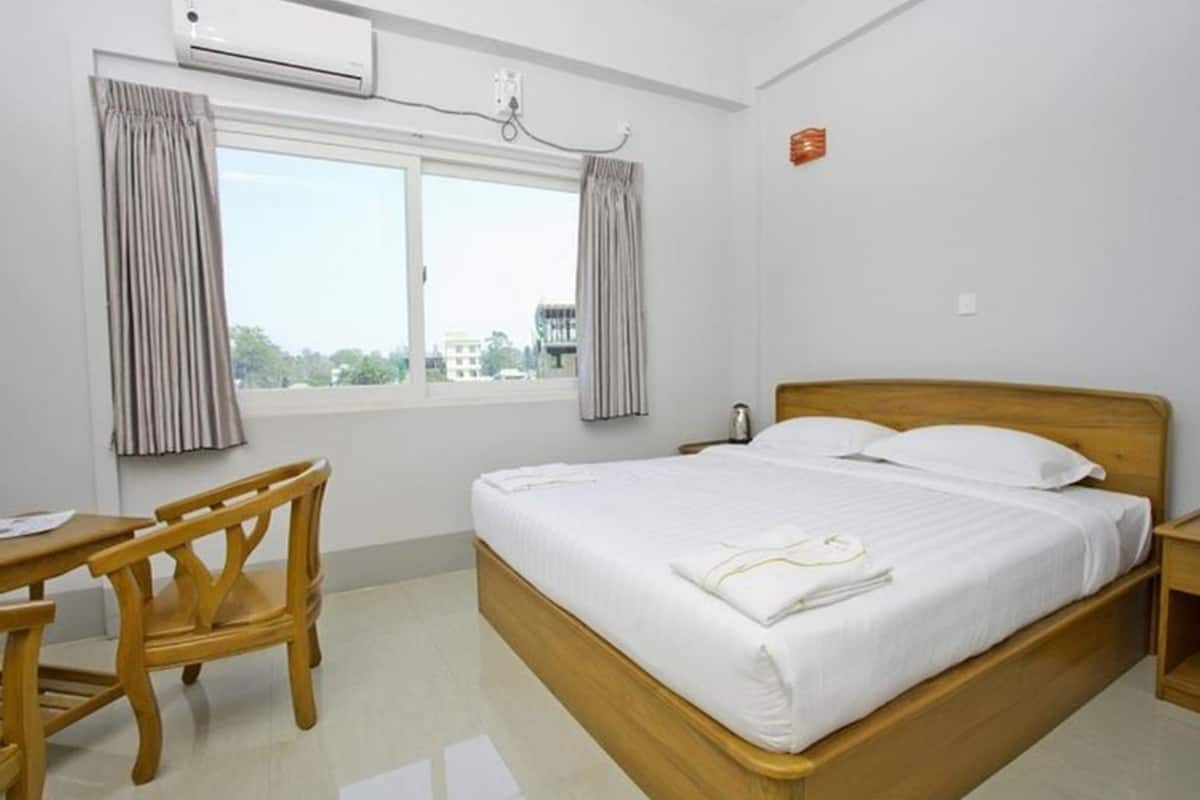 A hotel room with a bed, a wooden chair, a desk, and a window with curtains.