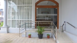 A hotel entrance with a glass door, a wooden archway, a metal staircase with handrails, and potted plants. - Hotel Maymyo (Pyin Oo Lwin)