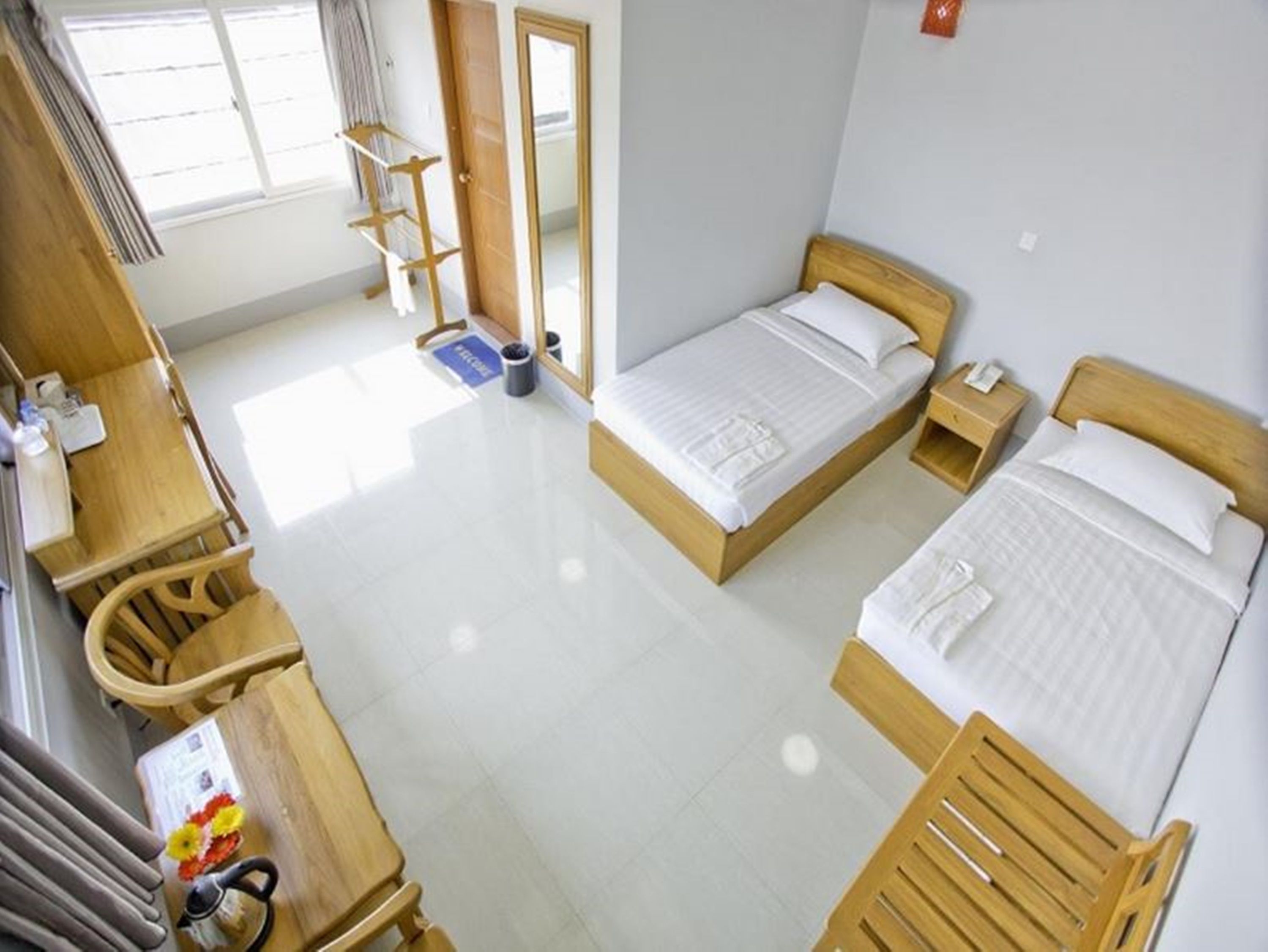 A hotel room with two beds, a wooden desk, a chair, a small table, and a mirror.