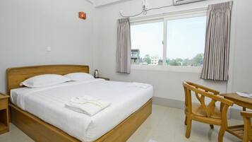 Habitación de hotel con cama de madera, un escritorio y una silla. Se observa una unidad de aire acondicionado en la pared y una ventana con cortinas.