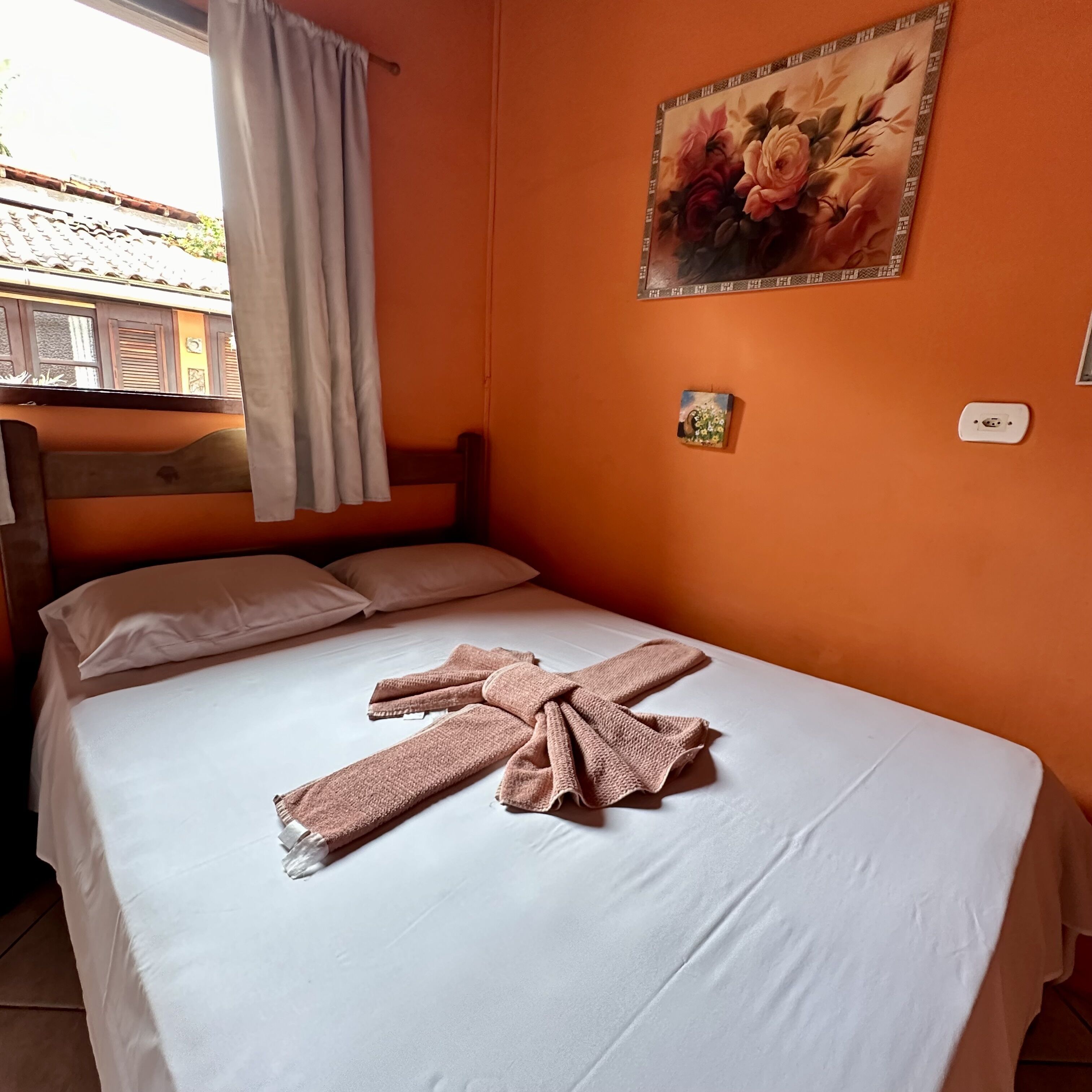A room with a bed, white bedding, a pink towel, a painting, and a window with curtains.