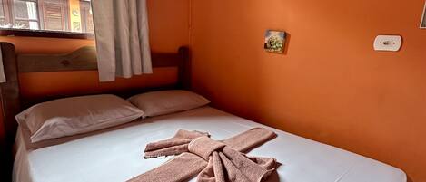 A room with a bed, white bedding, a pink towel, a painting, and a window with curtains.