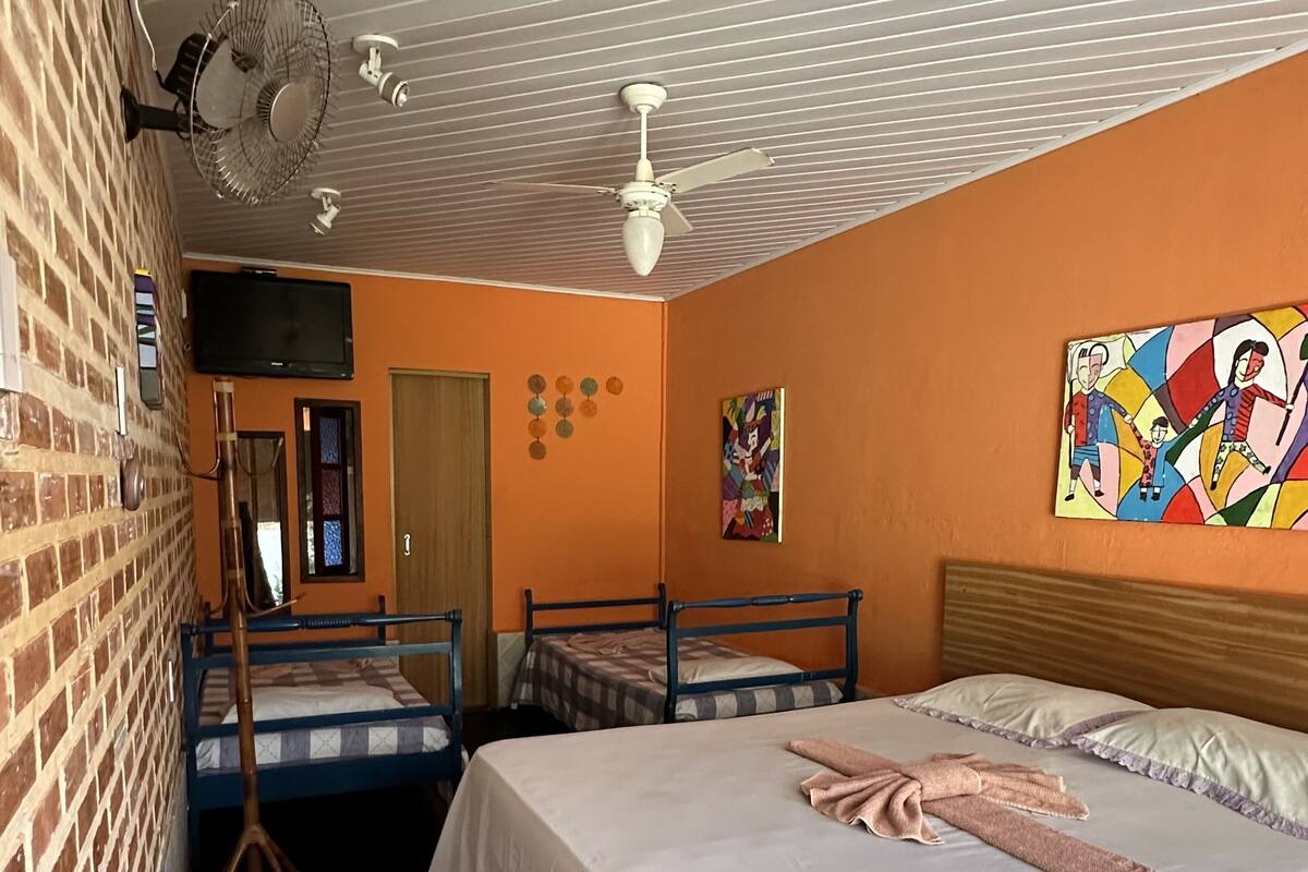 Ein Hotelzimmer mit zwei Einzelbetten, einem großen Bett, einem Deckenventilator, einem Fernseher und einer Backsteinwand.