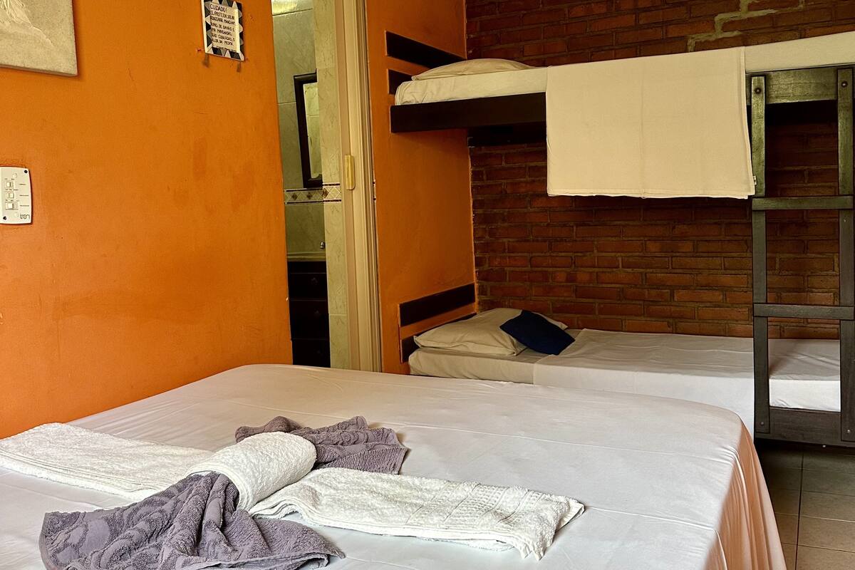Ein Zimmer mit zwei Betten, eines davon mit einem Schlafplatz darüber. Eine Tür führt ins Badezimmer, und an der Wand hängt ein Schild.