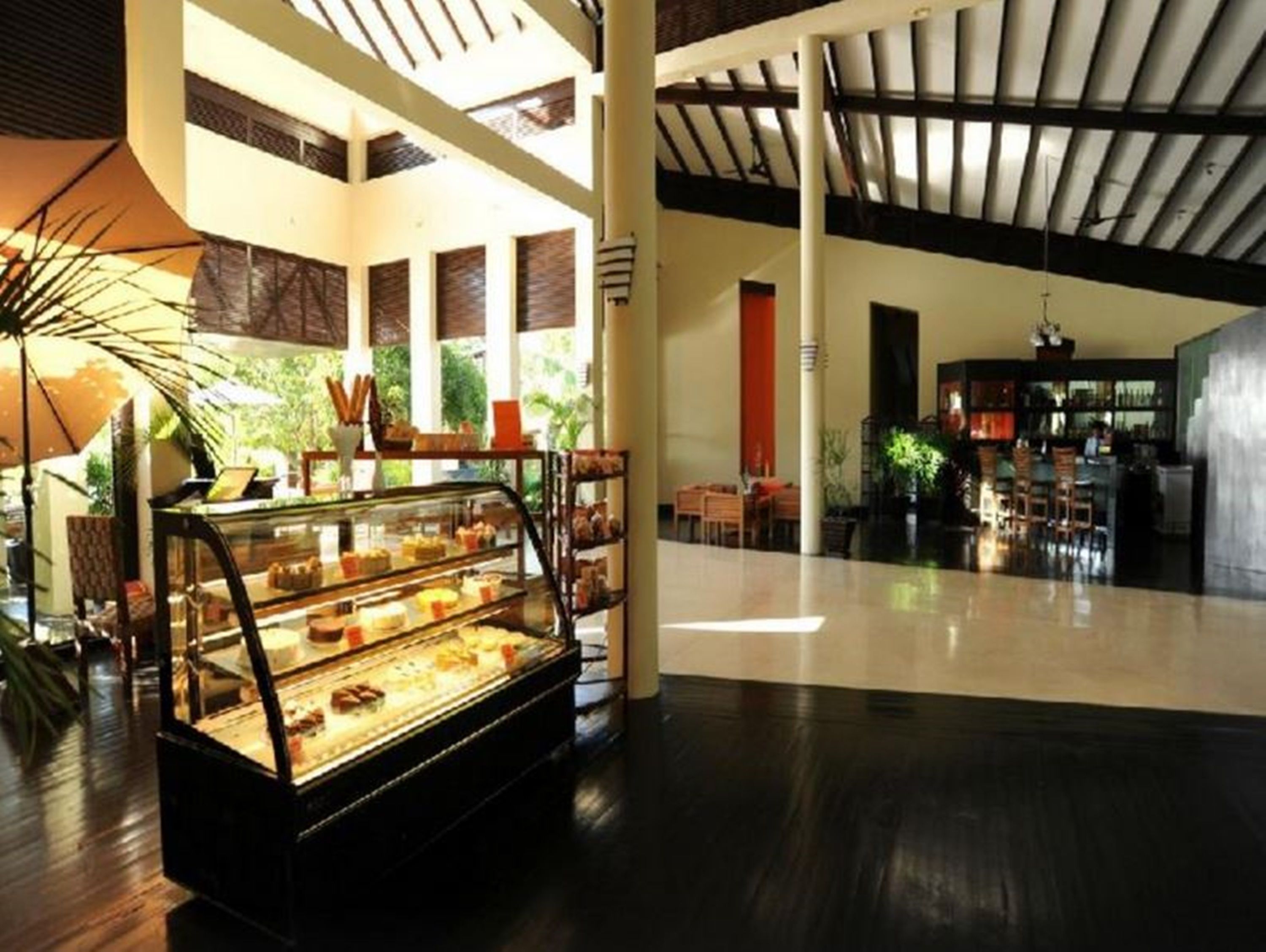 Un grand espace intérieur doté d’une vitrine centrale où sont exposées des pâtisseries, entouré de tables et de chaises.