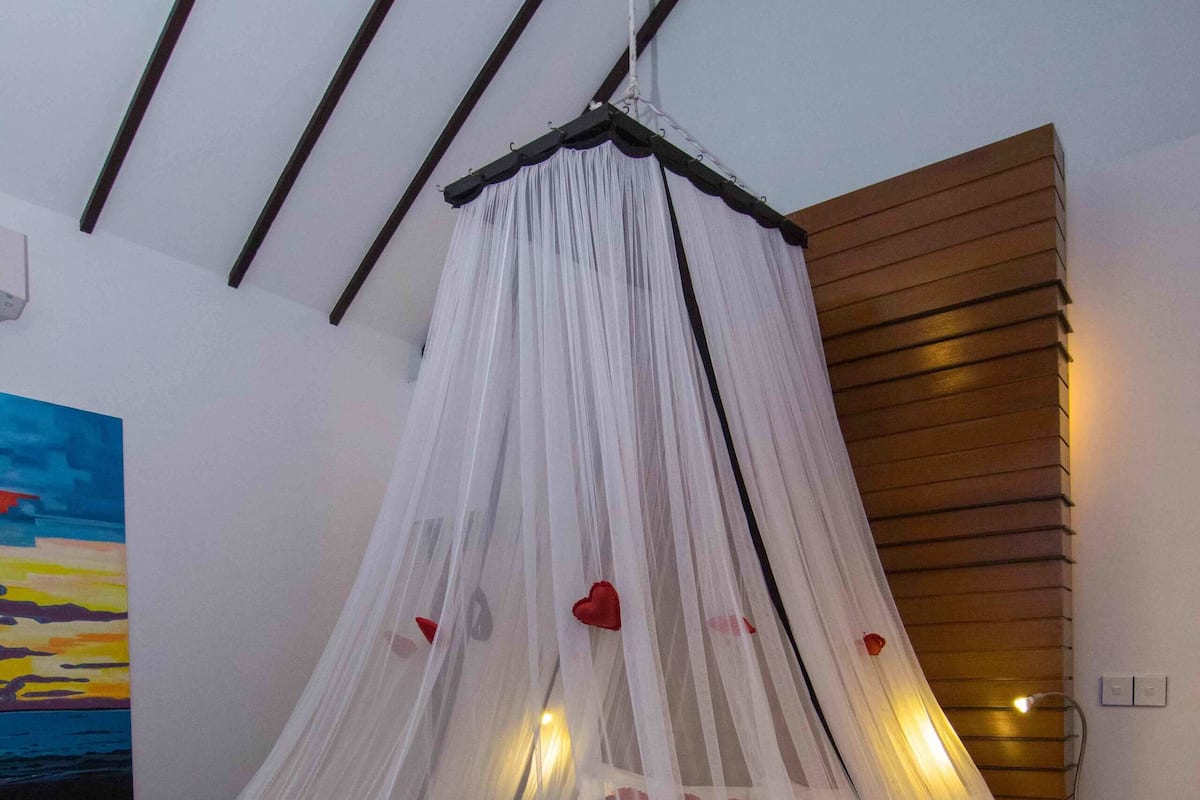 A bed with a white canopy, a painting on the wall, and a wooden panel on the wall.