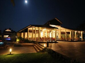 A well-lit outdoor dining area with a pool and a covered seating area.