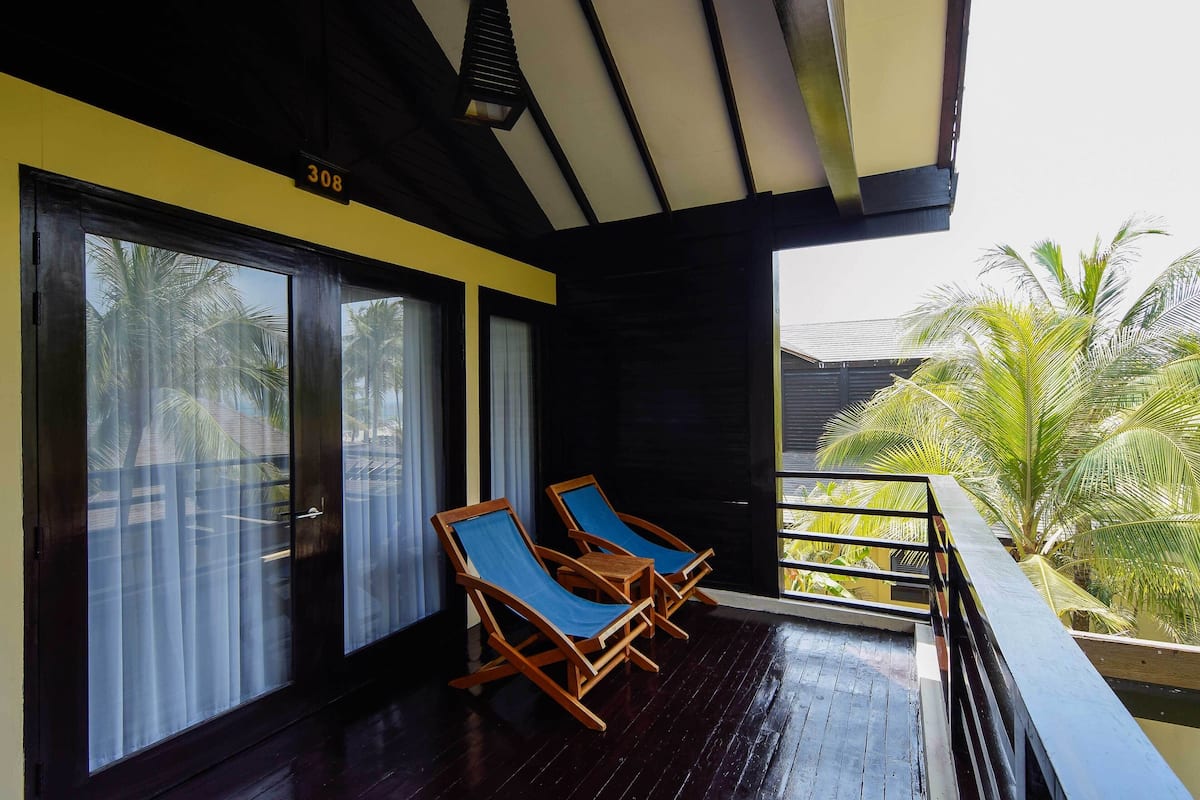 A balcony with two wooden lounge chairs and a view of palm trees.