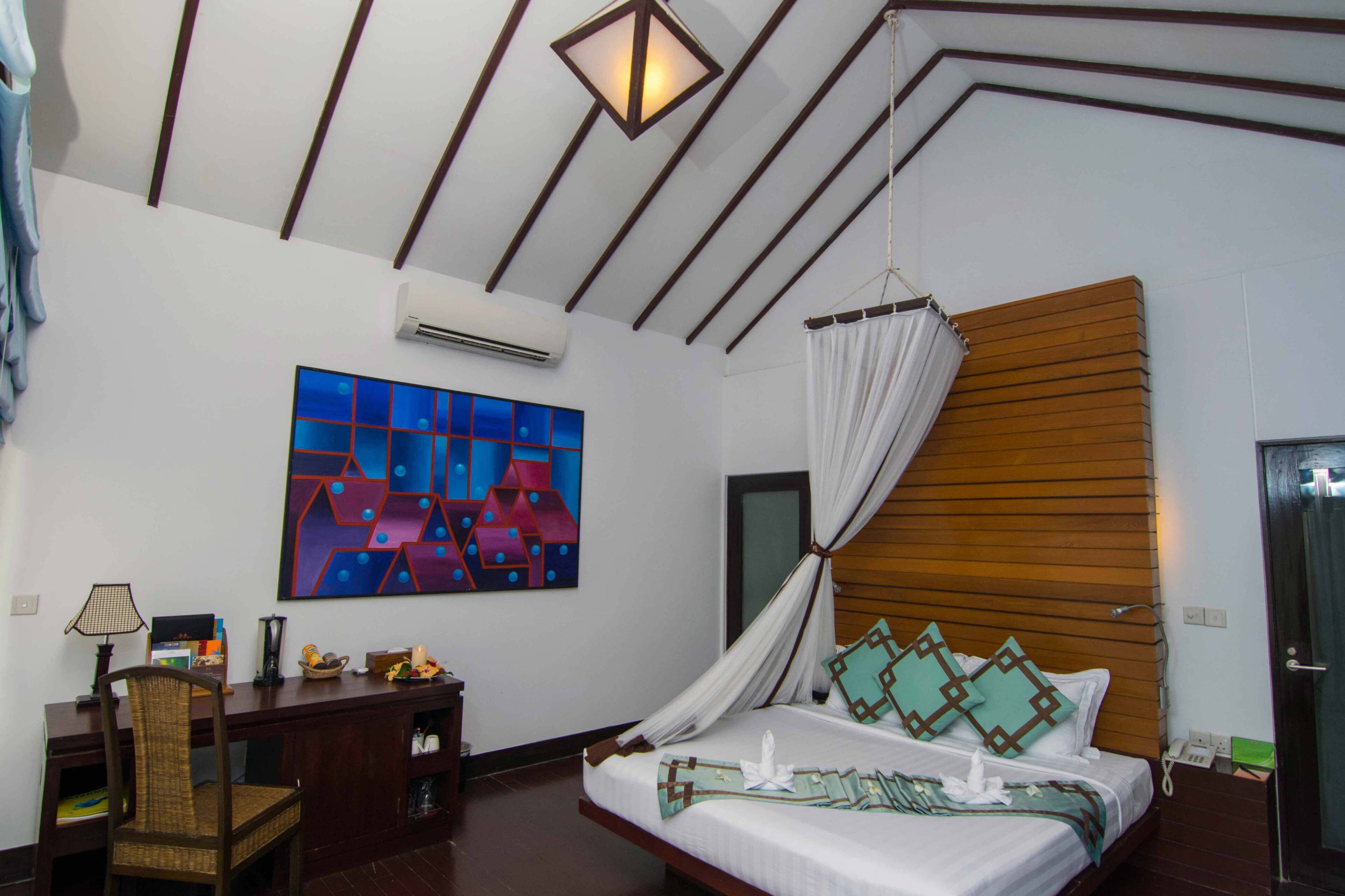 A bedroom with a bed, a desk with a chair, a painting, and a wooden headboard.