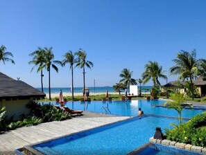 A pool area with lounge chairs, palm trees, and a view of the beach.
