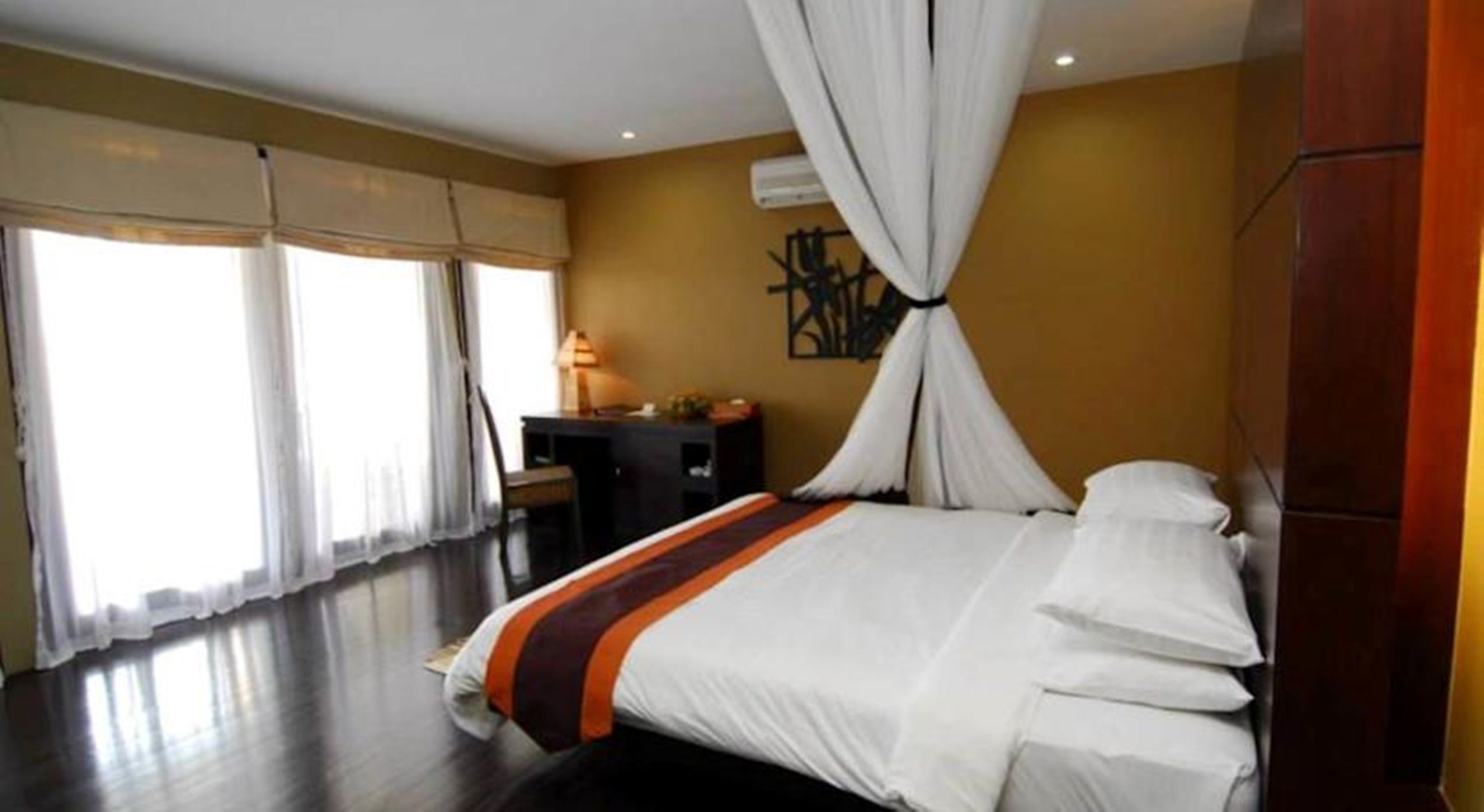 A hotel room with a bed, curtains, a desk, and a wall-mounted air conditioner.