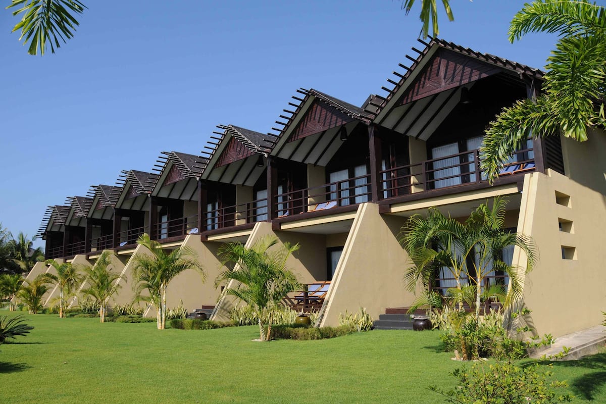 A row of modern, multi-story buildings with balconies, surrounded by well-maintained lawns and palm trees.
