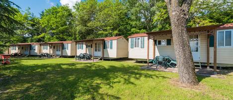 A row of mobile homes with a grassy yard and trees.