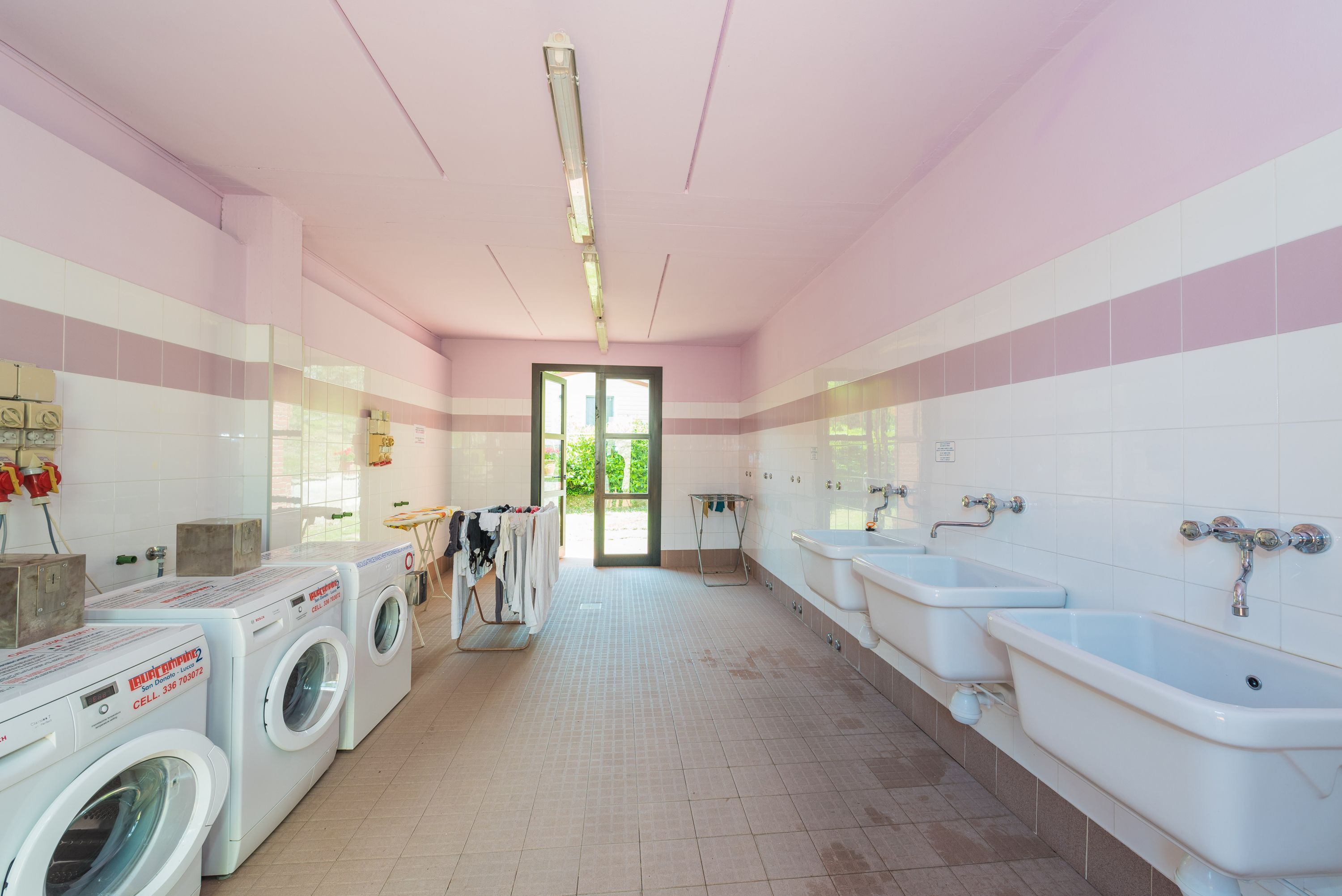 A laundry room with multiple washing machines, a drying rack, and two sinks.