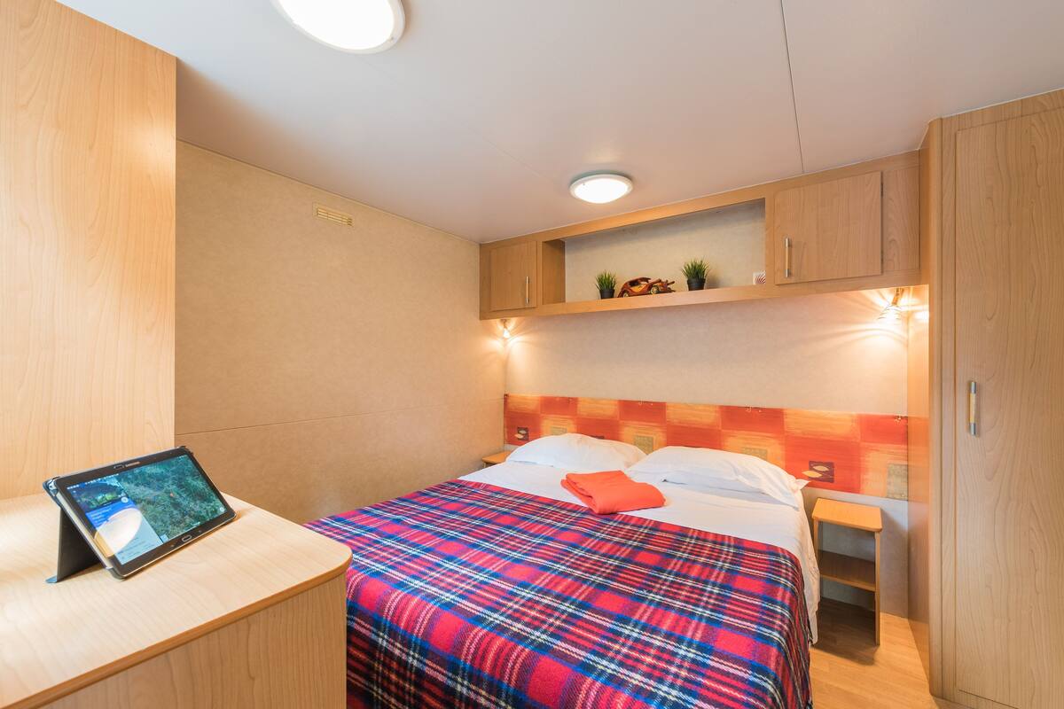 Une chambre à coucher bien rangée, avec un lit, une table de chevet, une tablette posée sur un support et une étagère au-dessus du lit.