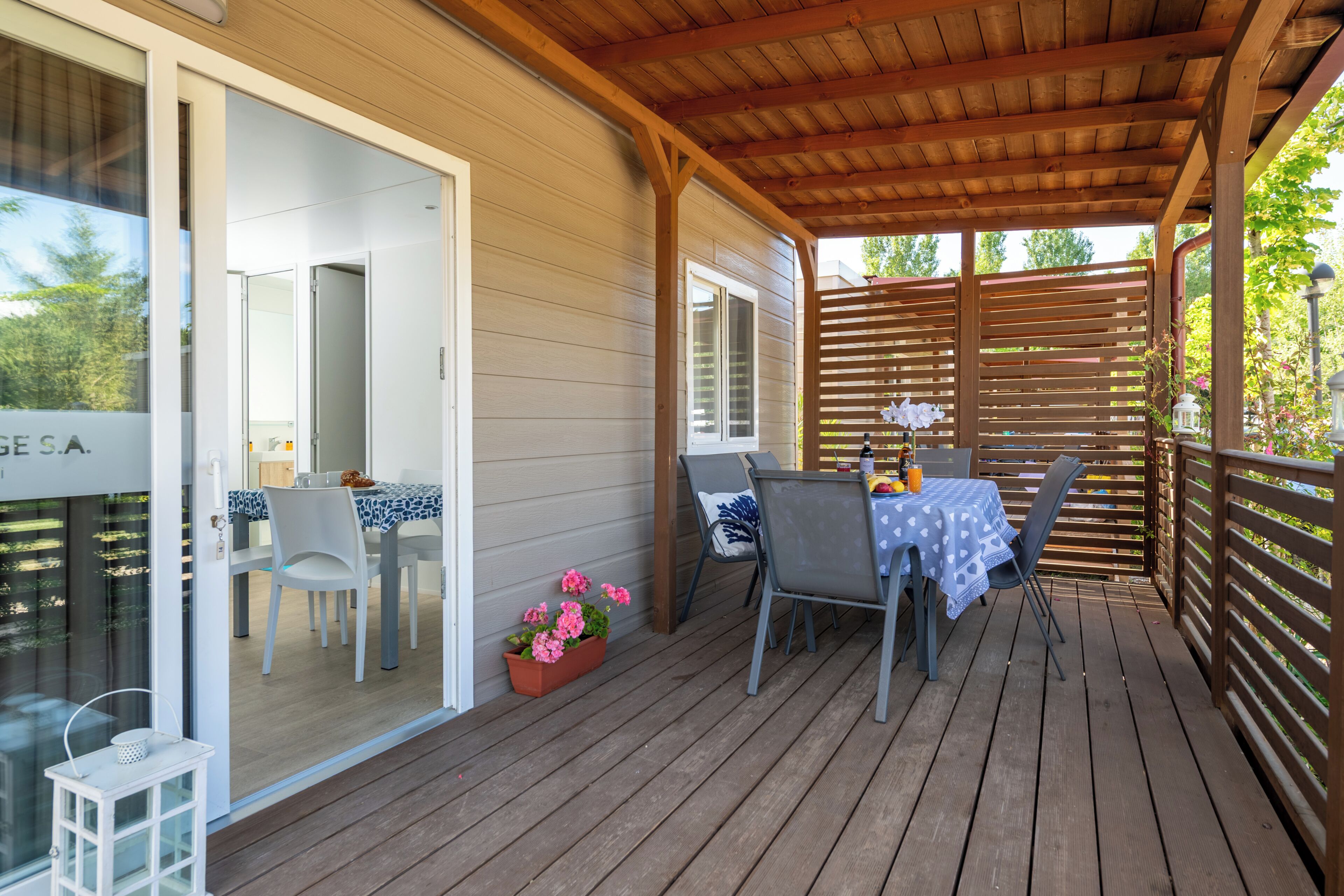Una terraza de madera con una mesa, sillas, una planta en maceta y vistas de la casa.
