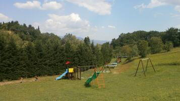 A playground with slides and swings in a grassy field with trees in the background.