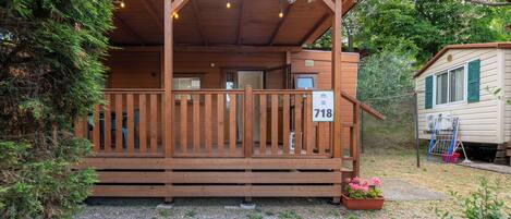 Een houten chalet met een veranda, een nummerbord en een kleine tuin.