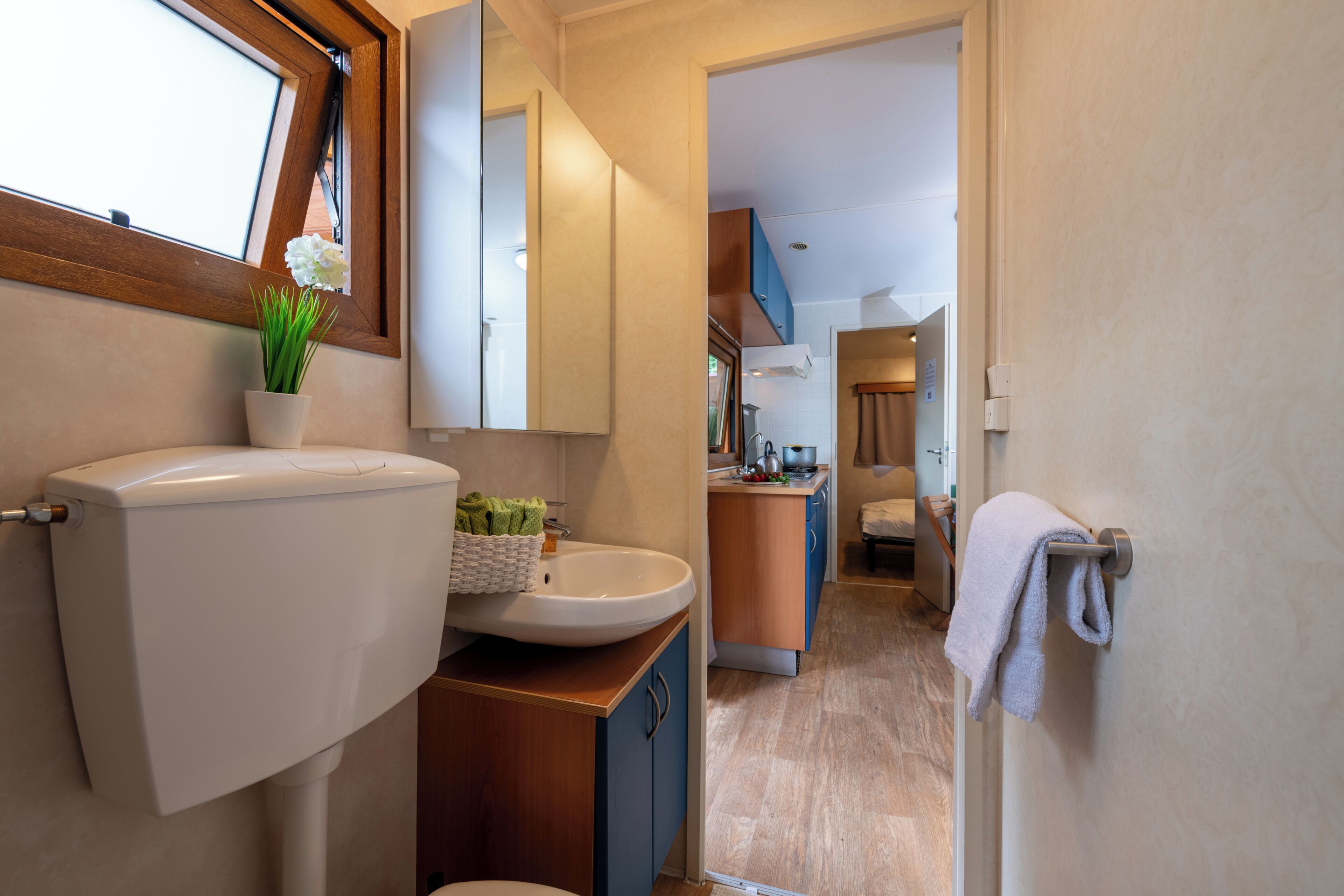 A modern bathroom with a toilet, sink, and mirror. There is a window with a view of the outside.