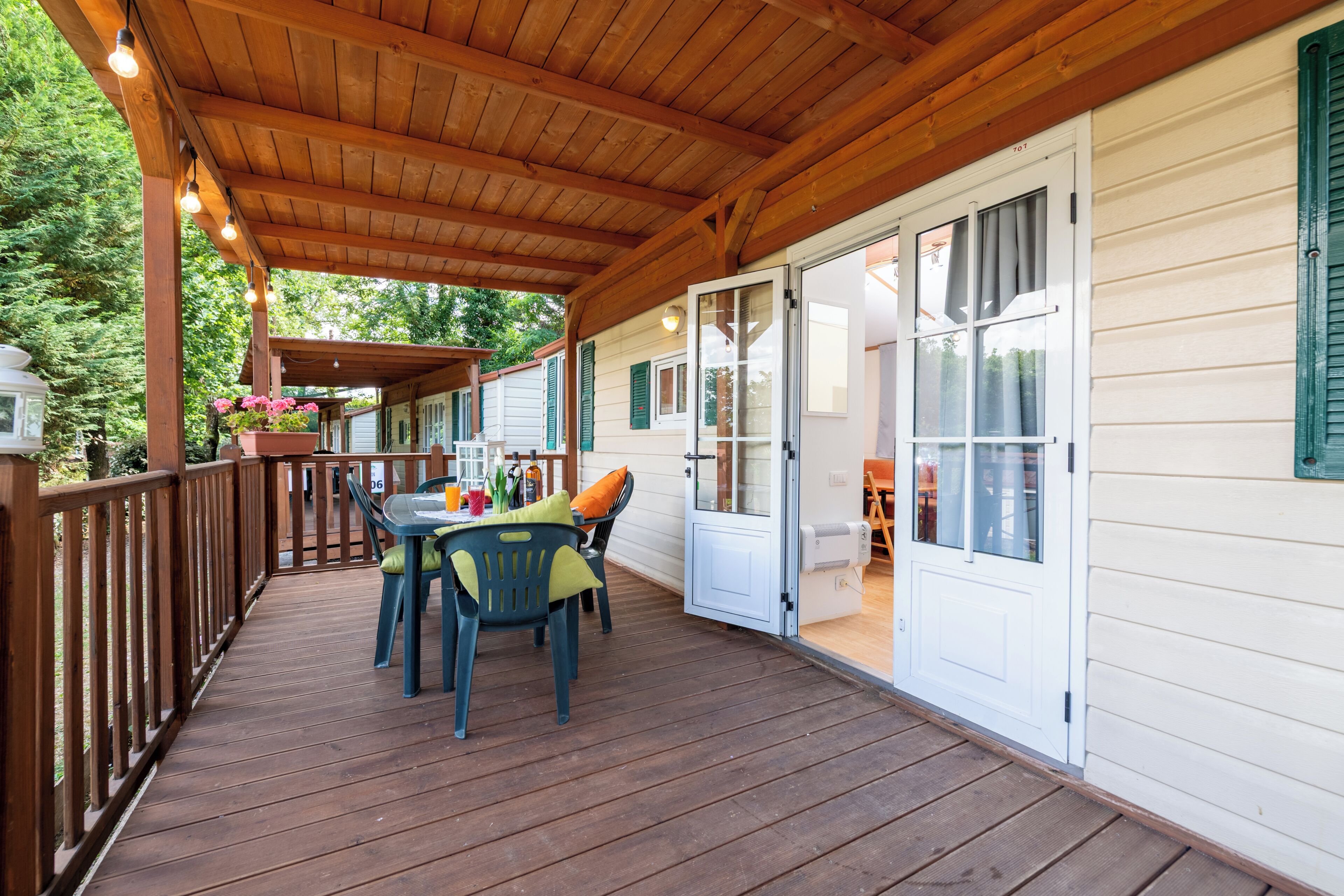 A covered wooden deck with a table and chairs, a white door, and a view of a house in the background.