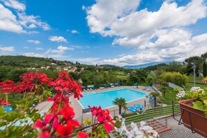 A swimming pool with lounge chairs, surrounded by greenery and hills in the background. - Camping Village Il Poggetto. (Rignano sull'Arno)