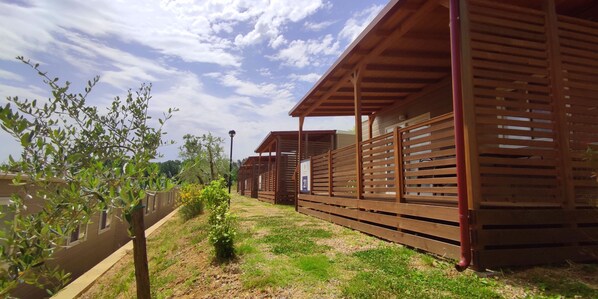 Une rangée de cabanes en bois, séparées par un sentier bordé de gazon.