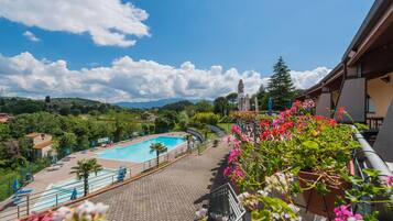 Vista d'una piscina envoltada de vegetació, amb cel blau i turons allunyats.