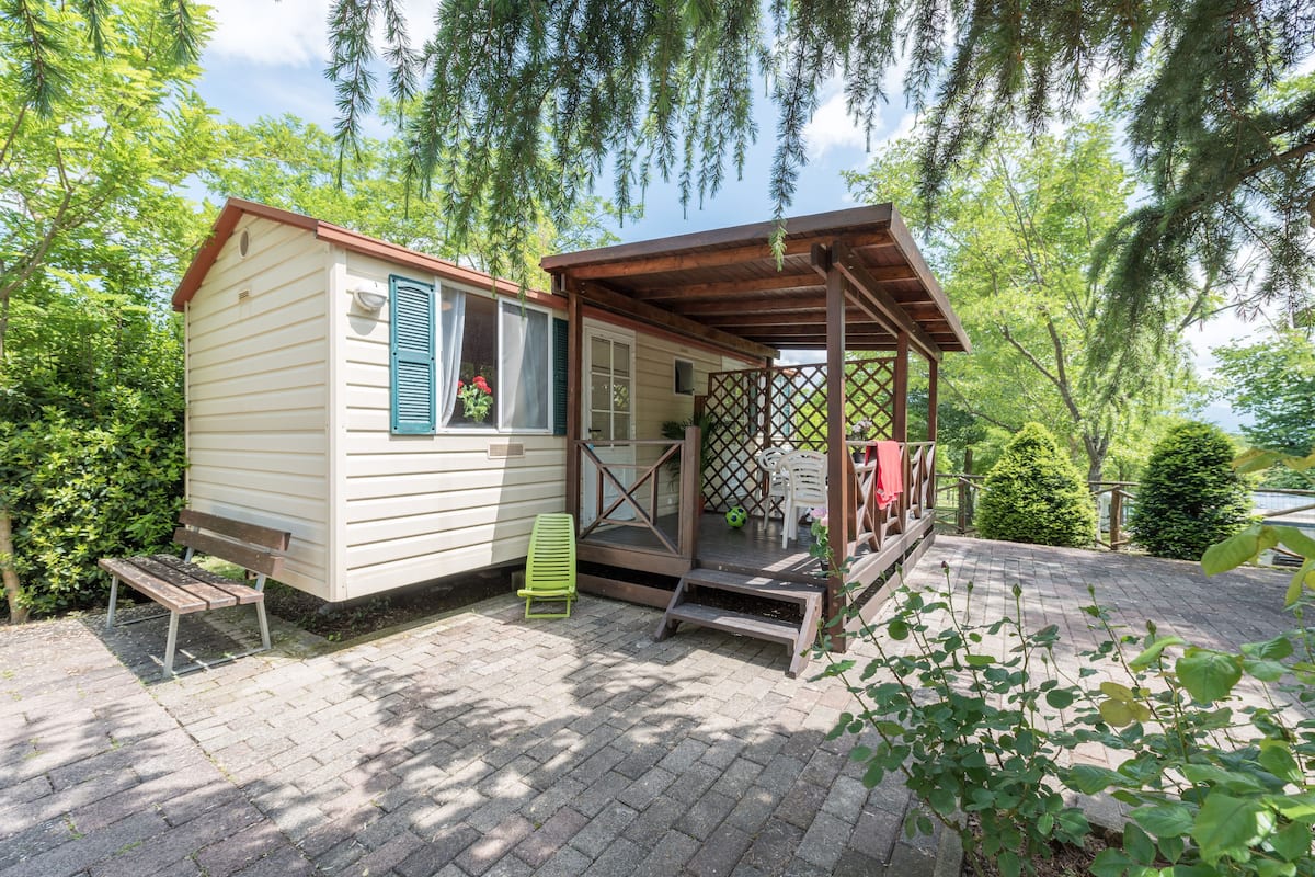 Une petite cabane avec une véranda, un banc et une chaise verte à l’extérieur.
