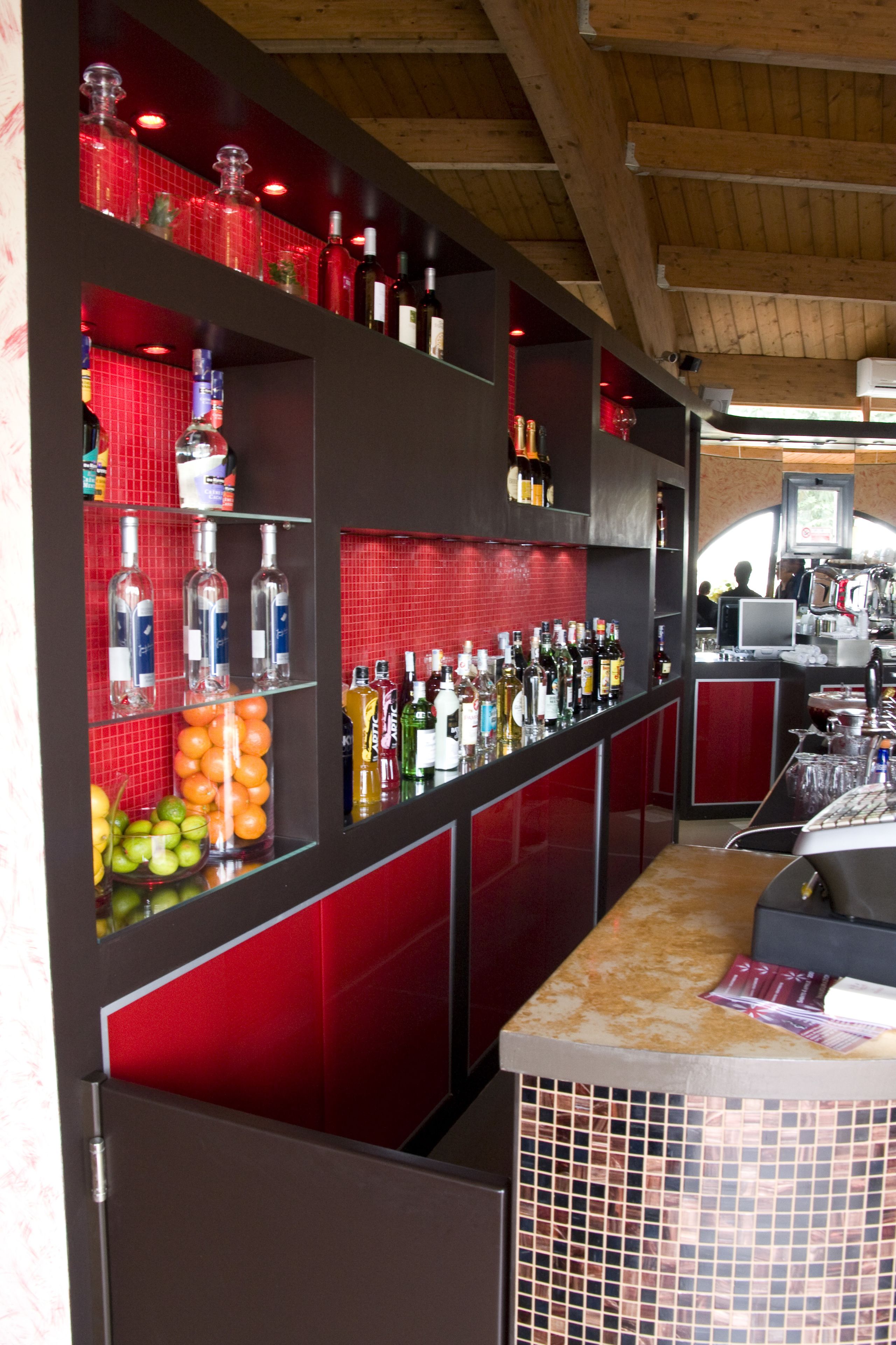 Una zona de bar con estantes llenos de botellas y vasos, una barra con un menú y un techo de madera.