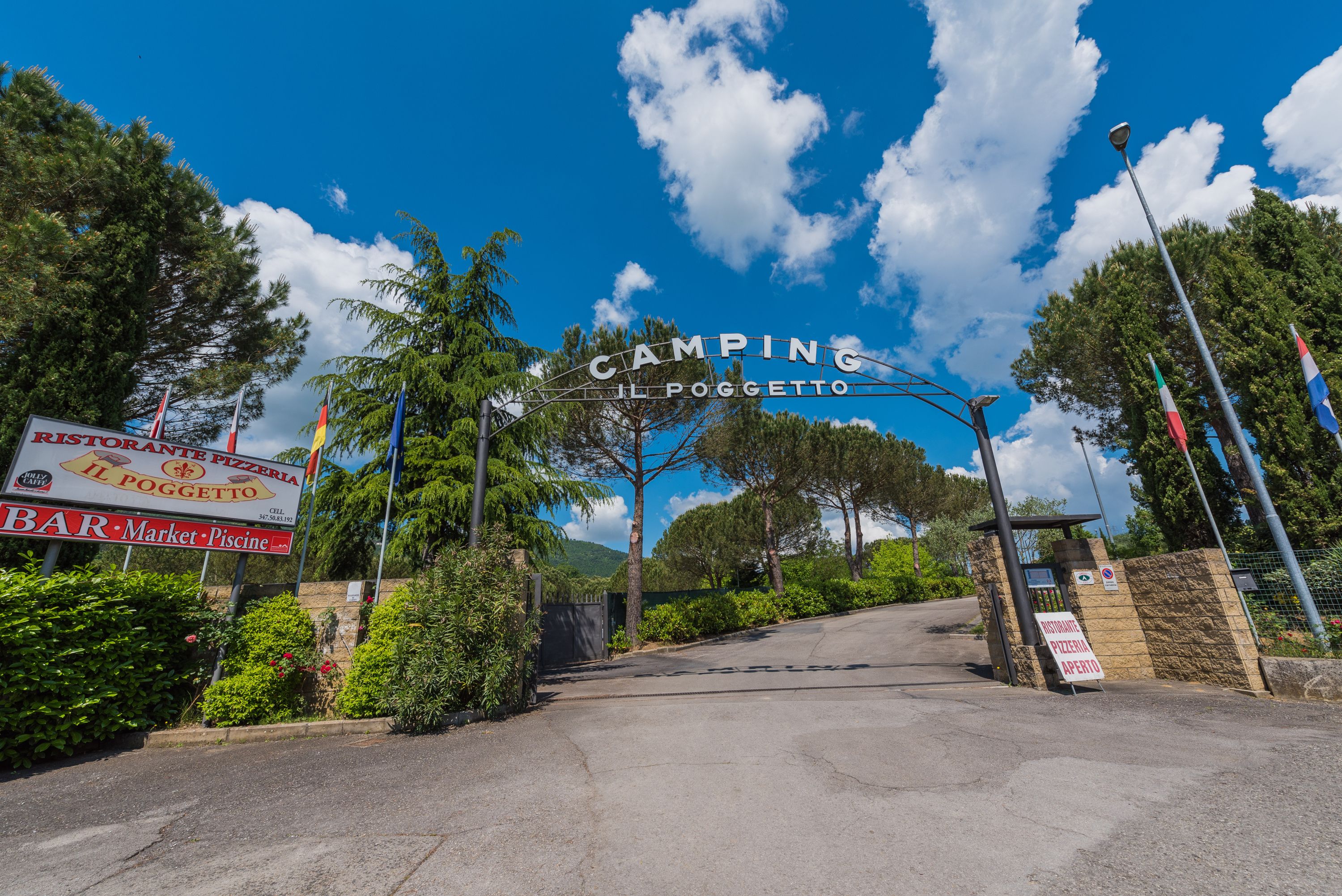 A sign for Camping Il Poggetto with a clear sky and trees in the background.