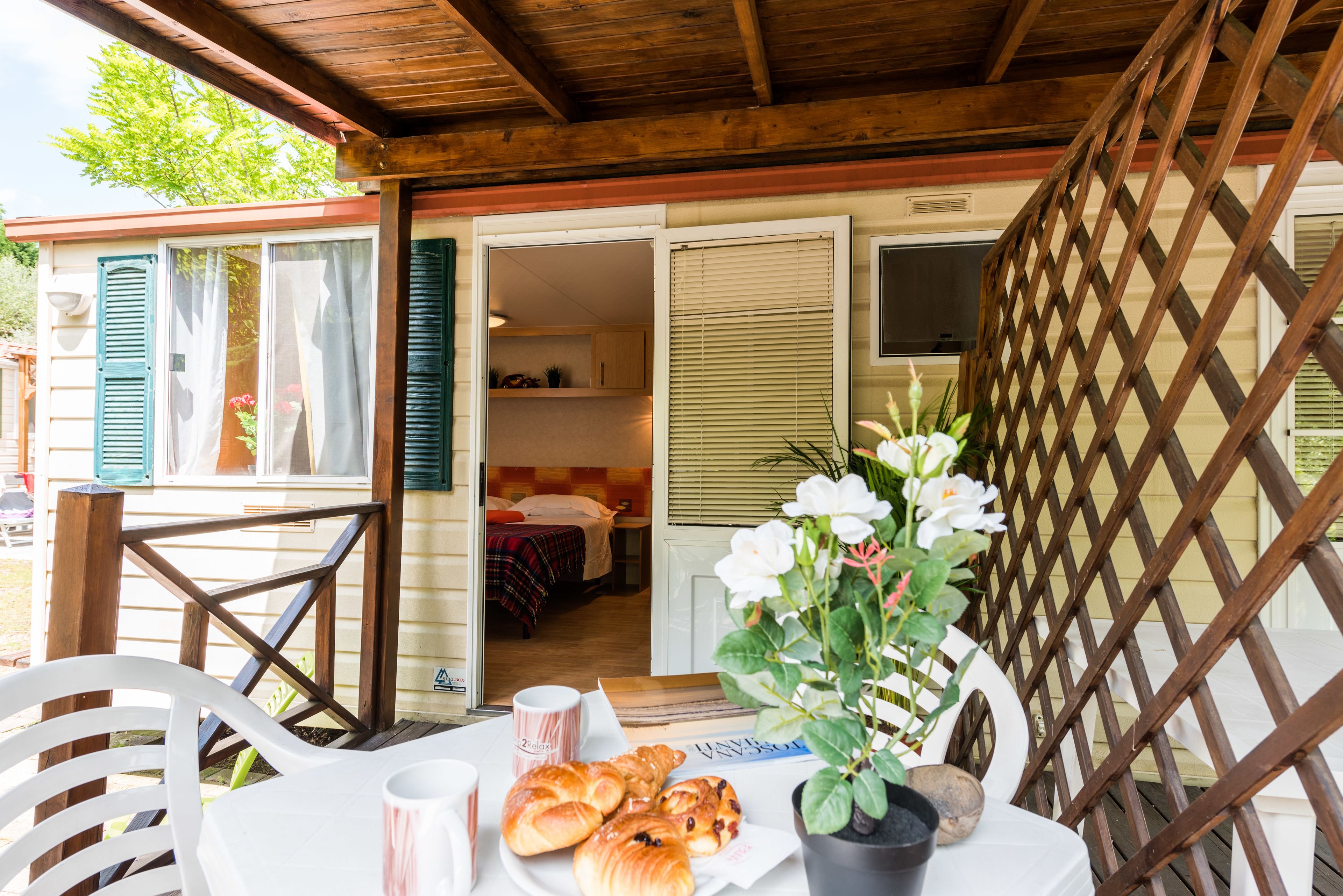 A cozy outdoor seating area with a table set for breakfast, a wooden lattice structure, and a glimpse into the adjacent room.