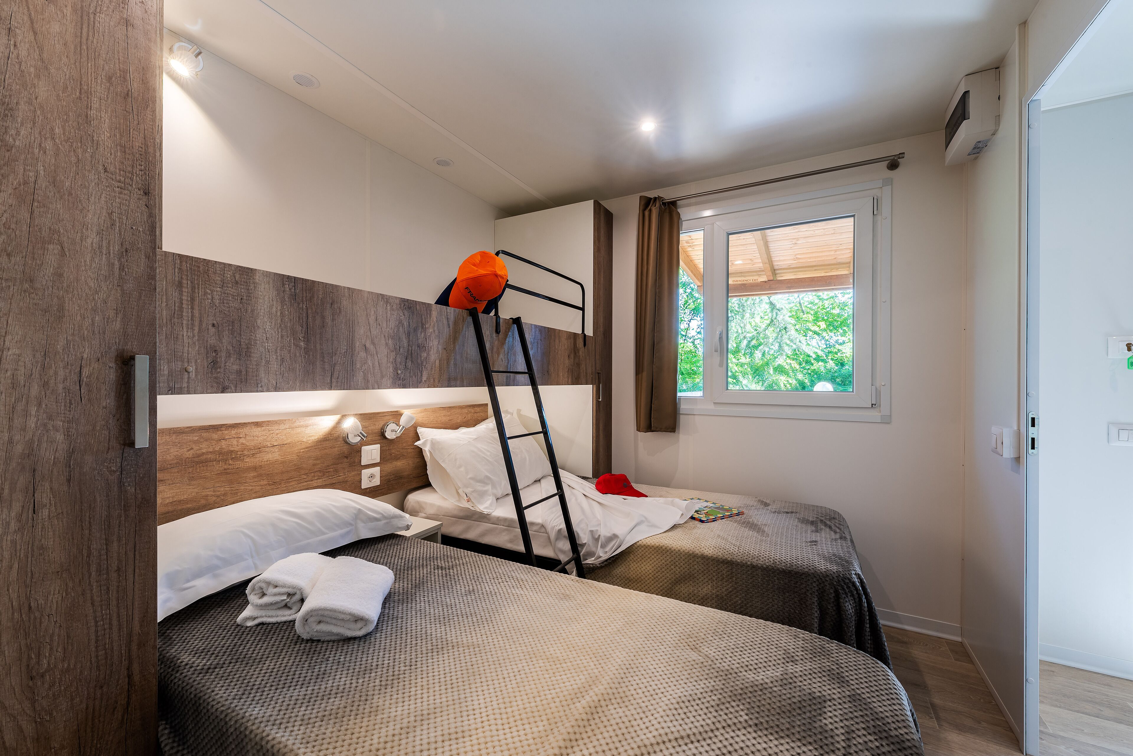 Une chambre avec deux lits, une échelle, une fenêtre avec des rideaux et un mur en bois.