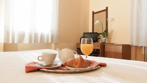 A neatly made breakfast table with a croissant, a cup of coffee, a glass of orange juice, and a teapot on a tray. - Hotel San Marco (Bedonia)