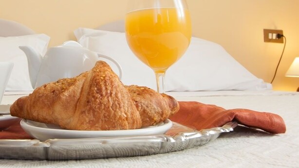 A breakfast setup on a bed with a croissant, a cup, and a glass of orange juice. - Hotel San Marco (Bedonia)